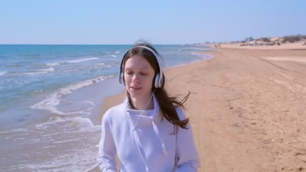 Жінка в навушниках музика біжить на морському піщаному пляжі спортивний біг тренування на відкритому повітрі . — стокове відео