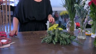 Kadın çiçekçi Satılık dükkanda buket için okaliptüs ve iris çiçekleri hazırlar.