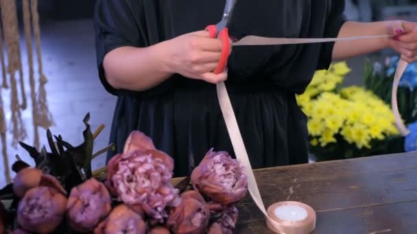Жінка-флорист вирізає стрічку, щоб зв'язати квітковий букет з коричневих півоній у квітковому магазині . — стокове відео