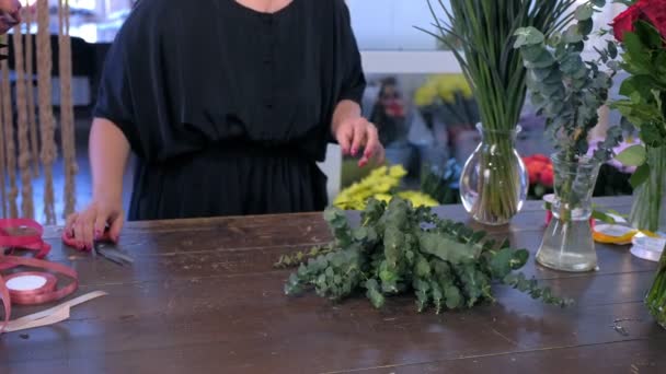 Mulher florista prepara flores de eucalipto e íris para buquê na loja à venda . — Vídeo de Stock