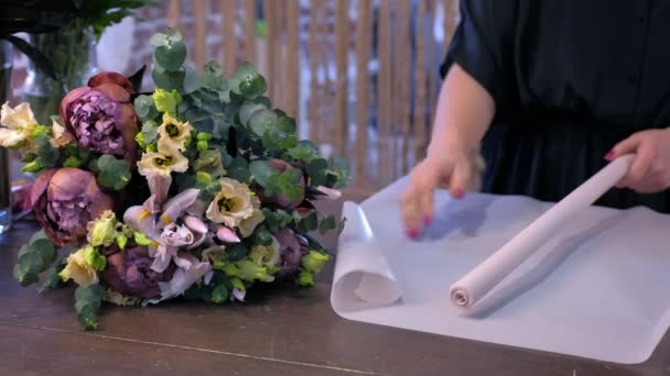 Bloemist maakt bloem boeket bereidt papier voor op verpakking in winkel, handen close-up. — Stockvideo