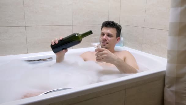 Müder Betrunkener liegt in Badewanne, gießt Wein aus einem Weinglas.