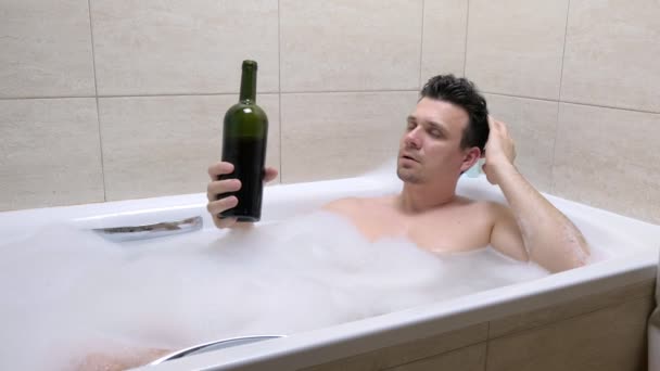 Tired 30s man in bath drinks wine from a bottle and falling asleep. — Stock Video