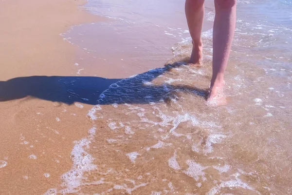 Descalço mulher turista caminha na água em ondas do mar praia de areia, pernas closeup . — Fotografia de Stock