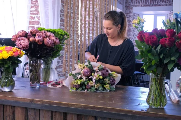 Florista mujer hace gran ramo de flores y lazos tallos de cinta en floristería . — Foto de Stock