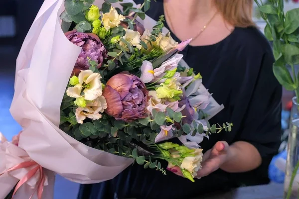 Mujer florista muestra gran ramo fruncido en papel blanco en la tienda, las manos de cerca . — Foto de Stock