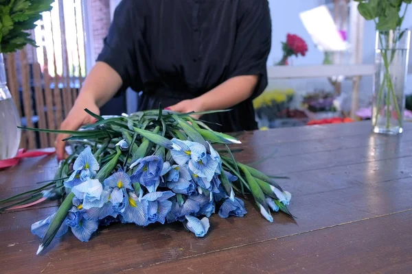 Γυναίκα ανθοπώλης prapares ίριδα λουλούδια για μπουκέτο σε φλοϊνιστικό κατάστημα στο ξύλινο τραπέζι. — Φωτογραφία Αρχείου
