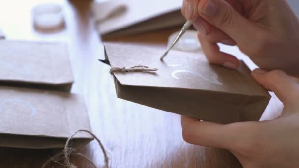 La mujer hace el calendario de Adviento de Navidad para los niños. Escribe un número en la bolsa por pincel y pintura blanca. Primer plano de las manos . — Vídeo de stock