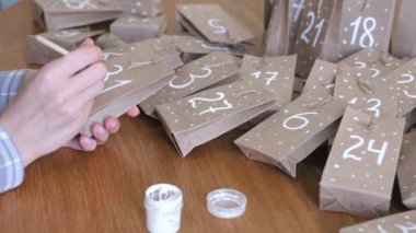 Kadın, çocuklar için Noel varış takvim yapar. Birkaç çanta üzerinde fırça ve beyaz boya ile yazar. Yakın çekim yakışıklı.