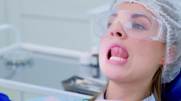 Νεαρή γυναίκα αγγίξει τα δόντια της με τη γλώσσα στην οδοντιατρική μετά τον καθαρισμό υπερήχων. — Αρχείο Βίντεο