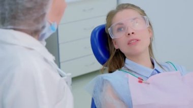 Stomatoloji kliniğinde diş hekimine diş problemleri hakkında konuşan hasta kadın.