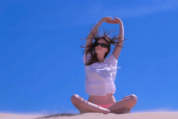 Mujer estiramiento se sienta pose de loto playa de arena manos hasta inclinaciones en el cielo día ventoso lateral . — Foto de Stock
