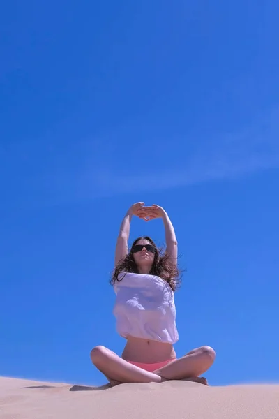Woman stretch yoga practice sits lotus pose sandy beach hands up windy day sky.