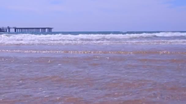 Riva del mare con grandi onde lunghe e molo in spiaggia di sabbia a soleggiata giornata ventosa . — Video Stock