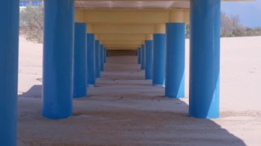 Kum sahilde köprü nün altından görünüm, paralel mavi sütunlar köprü tutun.