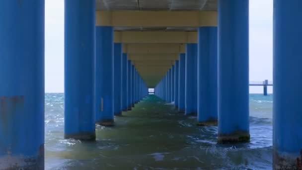 Meer unter Pier zwischen parallelen blauen Säulen, die einen schmalen Korridor im Wasser bilden. — Stockvideo
