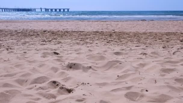 Spiaggia di sabbia marina con onde tempestose e vista sul molo nella soleggiata giornata ventosa . — Video Stock