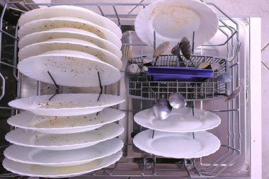 Bulaşık makinesi sepetinde beyaz kirli tabaklar ve kaşık.