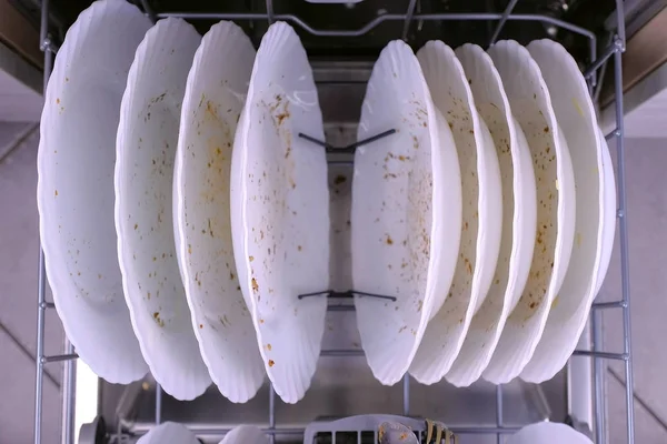 Placas brancas sujas em máquina de lavar louça e empurra a cesta com utensílios de cozinha . — Fotografia de Stock