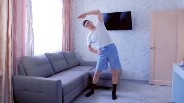 Engraçado nerd homem está fazendo inclinações para os lados exercício em casa na sala de estar. Engraçado puxa shorts durante o exercício . — Vídeo de Stock