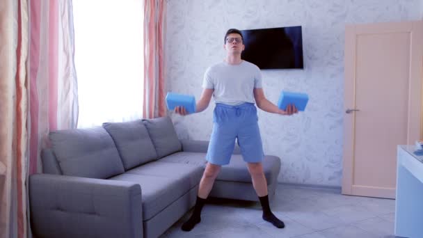 Homem nerd engraçado está fazendo exercícios para bíceps de mão com blocos de ioga em vez de halteres em casa. Conceito de humor esportivo . — Vídeo de Stock