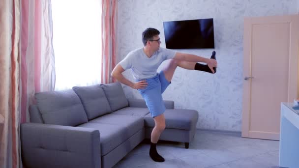 Homme nerd drôle fait des exercices d'étirement pour la jambe, en essayant de soulever sa jambe vers le haut, et en tombant par terre à la maison. Concept d'humour sportif . — Video