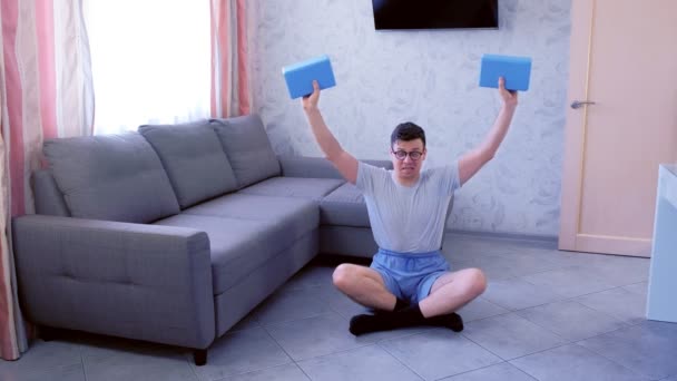Faible nerd homme fait des exercices pour les mains avec des blocs de yoga au lieu d'haltères. Concept d'humour sportif . — Video