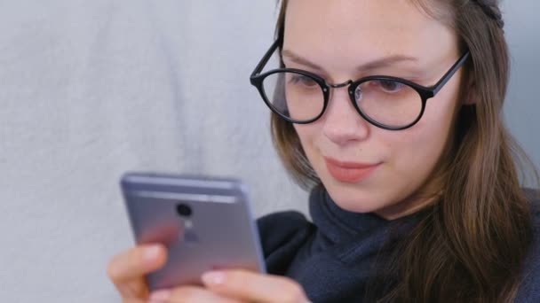 Glad ung brunett kvinna i glas typer ett meddelande på en mobiltelefon. — Stockvideo