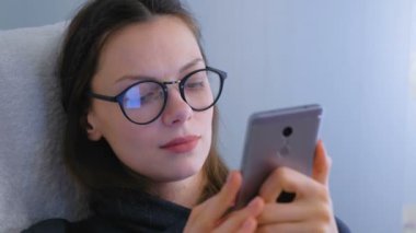 Gözlüklü genç esmer kadın cep telefonunda bir mesaj türleri.