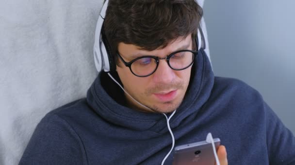 Homem ouve música em fones de ouvido no smartphone e canta uma música. Tempo de relaxamento . — Vídeo de Stock