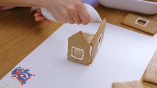 Womans kezet, hogy mézeskalács ház ragasztások részleteit a cukor édes jegesedés. Főzés házi mézeskalács ház. — Stock videók
