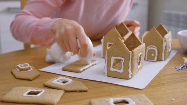 Las manos femeninas hacen casas de pan de jengibre pega detalles con azúcar dulce glaseado. Cocinar casa casera de jengibre . — Vídeos de Stock