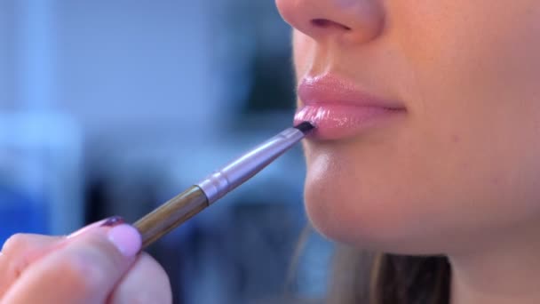 Maquillaje artista aplica brillo de labios utiliza cepillo en los labios modelo chica compone maquillaje . — Vídeos de Stock