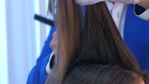 Les mains de styliste de cheveux travaillent avec le fer à lisser chaud d'utilisation de cheveux de fille, faisant des boucles . — Video