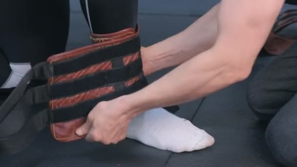 Entrenador pone fijadores pierna deportista se prepara para el estiramiento miofascial en el gimnasio . — Vídeo de stock