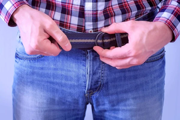 Man is putting on the belt on his jeans, waist and hands closeup.