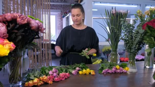 Florista prepara flores para cacho corta rosa espinhos sobre mesa na loja de flores . — Vídeo de Stock