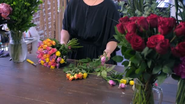 Florist woman works makes bouquet from colourful roses in shop, hands closeup. — Stock Video