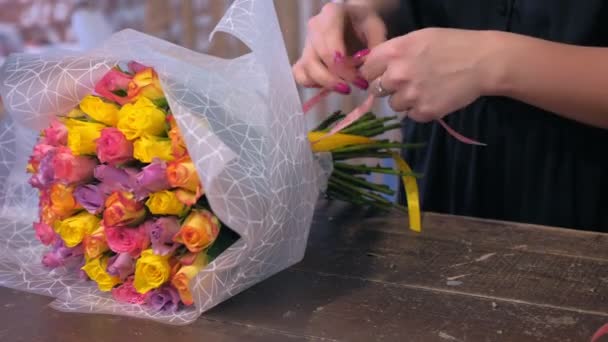 Donna fiorista packaging bouquet di rose in carta in negozio di fiori, mani primo piano . — Video Stock