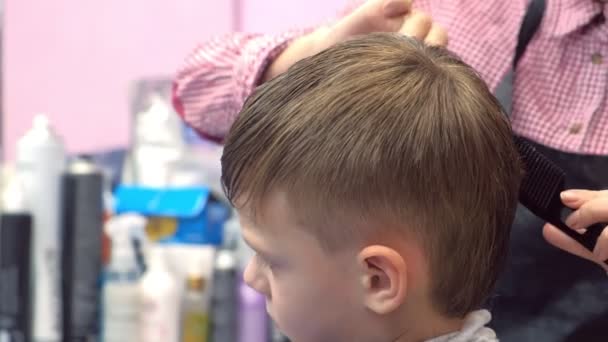 Перукар розрізає волосся ножицями на голові хлопчиків. Вид збоку, стилісти руки крупним планом . — стокове відео
