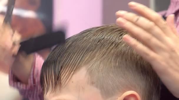 Hairdresser is going to cut bangs with scissors on boys head. Stylists hands close-up. — Stock Video