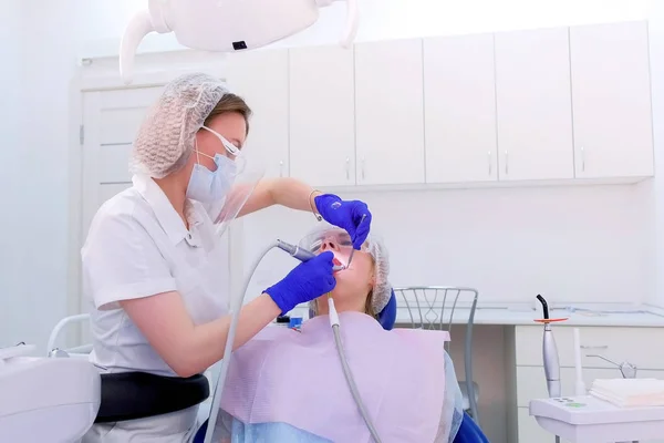 Dental hygienist cleaning and brushing womans teeth uses drill with brush.