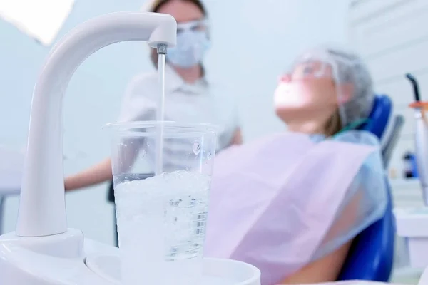 Pouring water in glass in stomatology clinic on doctor and patient background. — Stock Photo, Image