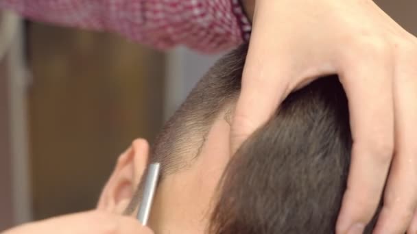 Barber se rase les cheveux sur les tempes mans avec un rasoir pointu. Stylistes mains close-up. — Video