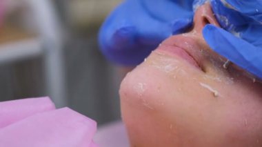 Güzellik uzmanı kadın yüzünü kaldırır ve maskeyi yuvarlar. Temizlik yüzü. Çene ve burun yakın çekim.