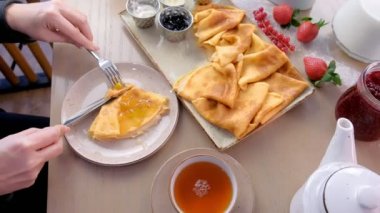 Kadın Rus geleneksel krep yiyor blini hizmet reçel, ekşi krema ve çilek plaka üzerinde. Ve içecek çay. Yakın çekim yan görünüm.