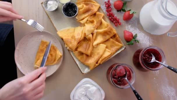 여자는 접시에 잼, 사워 크림, 딸기와 함께 제공되는 러시아 전통 팬케이크를 먹고있다. 클로즈업 상단 보기. — 비디오