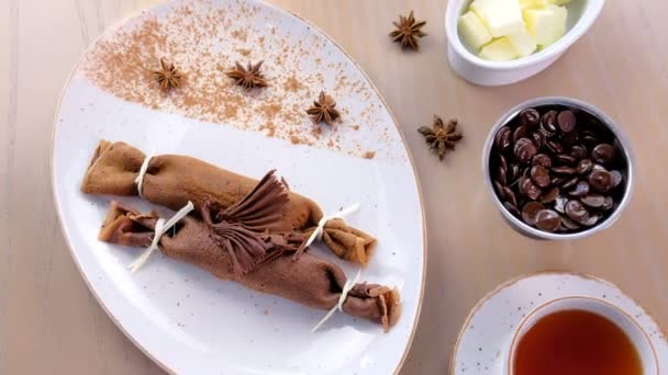 Chocolade Russische pannenkoeken, blini met wrongel invullen op de plaat. Geserveerd met een kopje thee en chocolade. Bovenaanzicht. — Stockvideo