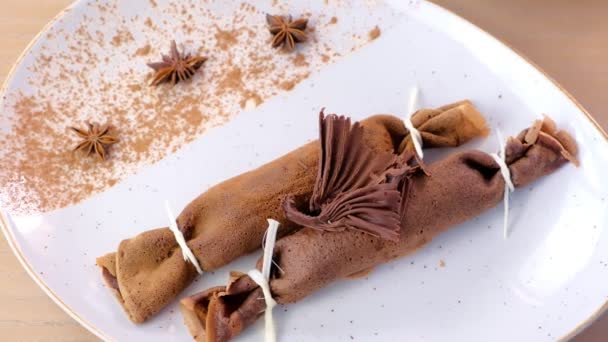 Frittelle russe al cioccolato, blini con ripieno di cagliata sul piatto. Servito con una figura di cioccolato . — Video Stock