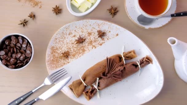 Chocolade Russische pannenkoeken, blini met wrongel invullen op de plaat. Geserveerd met een kopje thee en boter. Bovenaanzicht. — Stockvideo